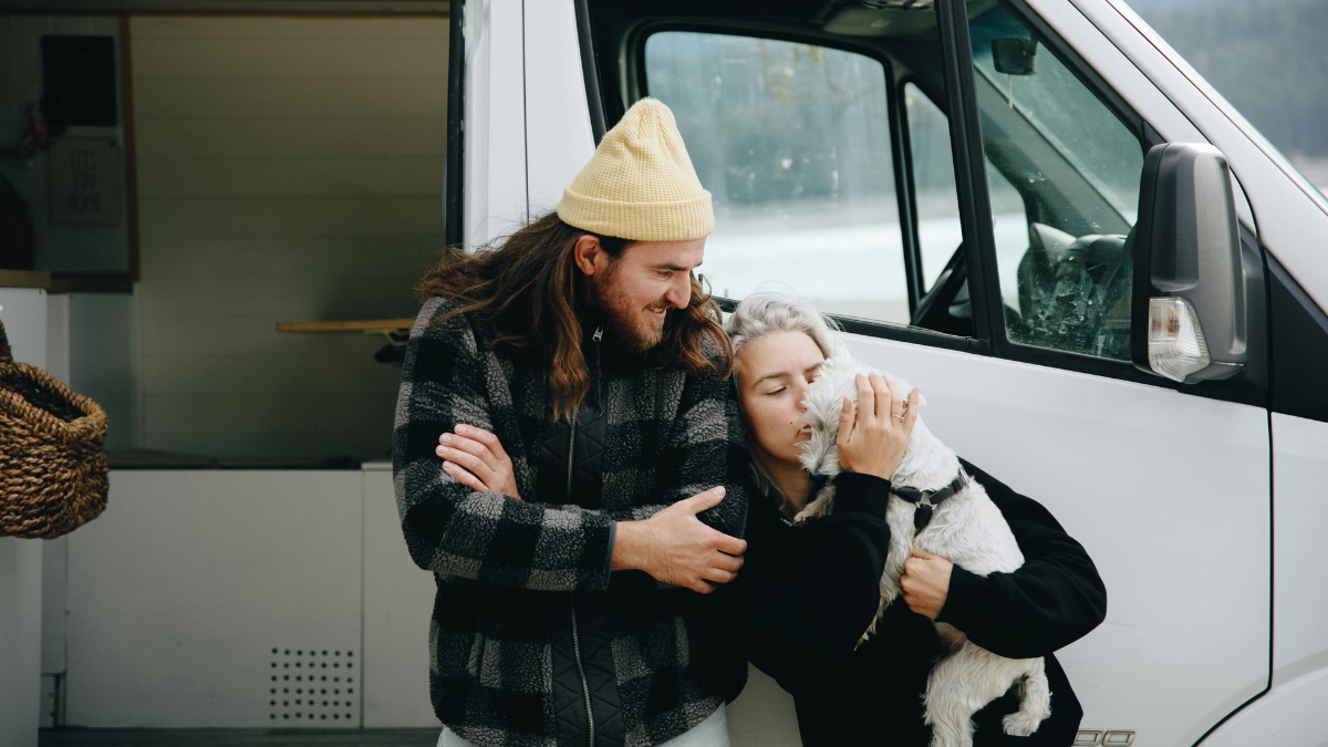 Couple cuddles their dog outside their camper van conversion