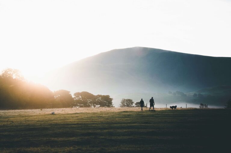A couple walk their dog across a field at sunrise in the Lake District