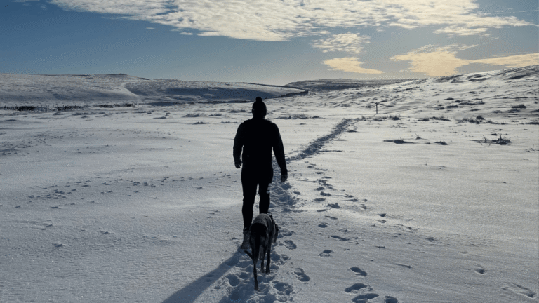 Man walks in the snow on a hike with his dog in Malham, Yorkshire Dales
