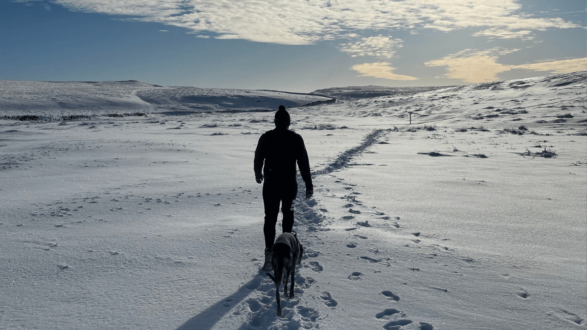 Man walks in the snow on a hike with his dog in Malham, Yorkshire Dales