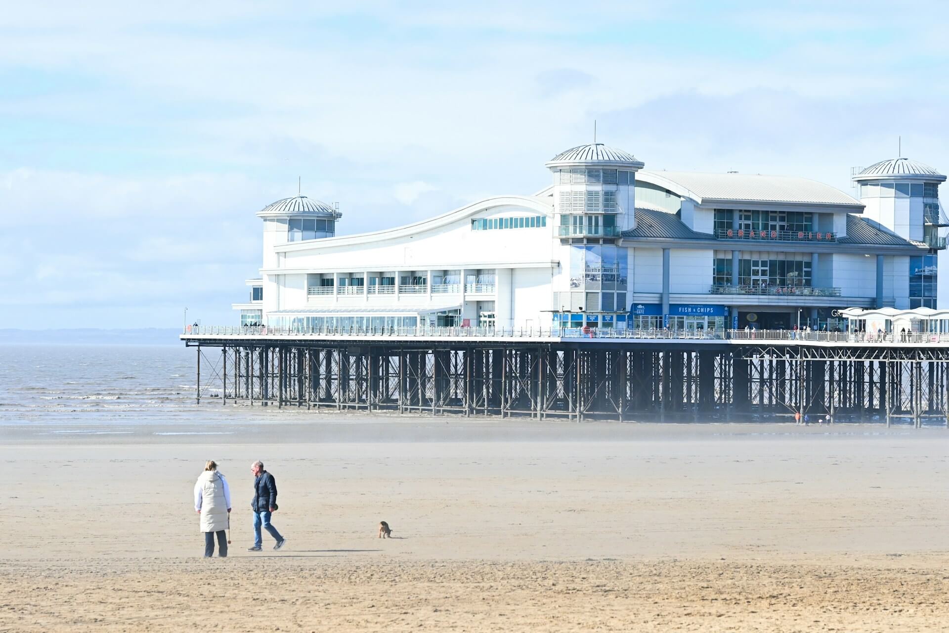 A couple walk their dog on a dog friendly beach in Weston-super-mare, Somerset