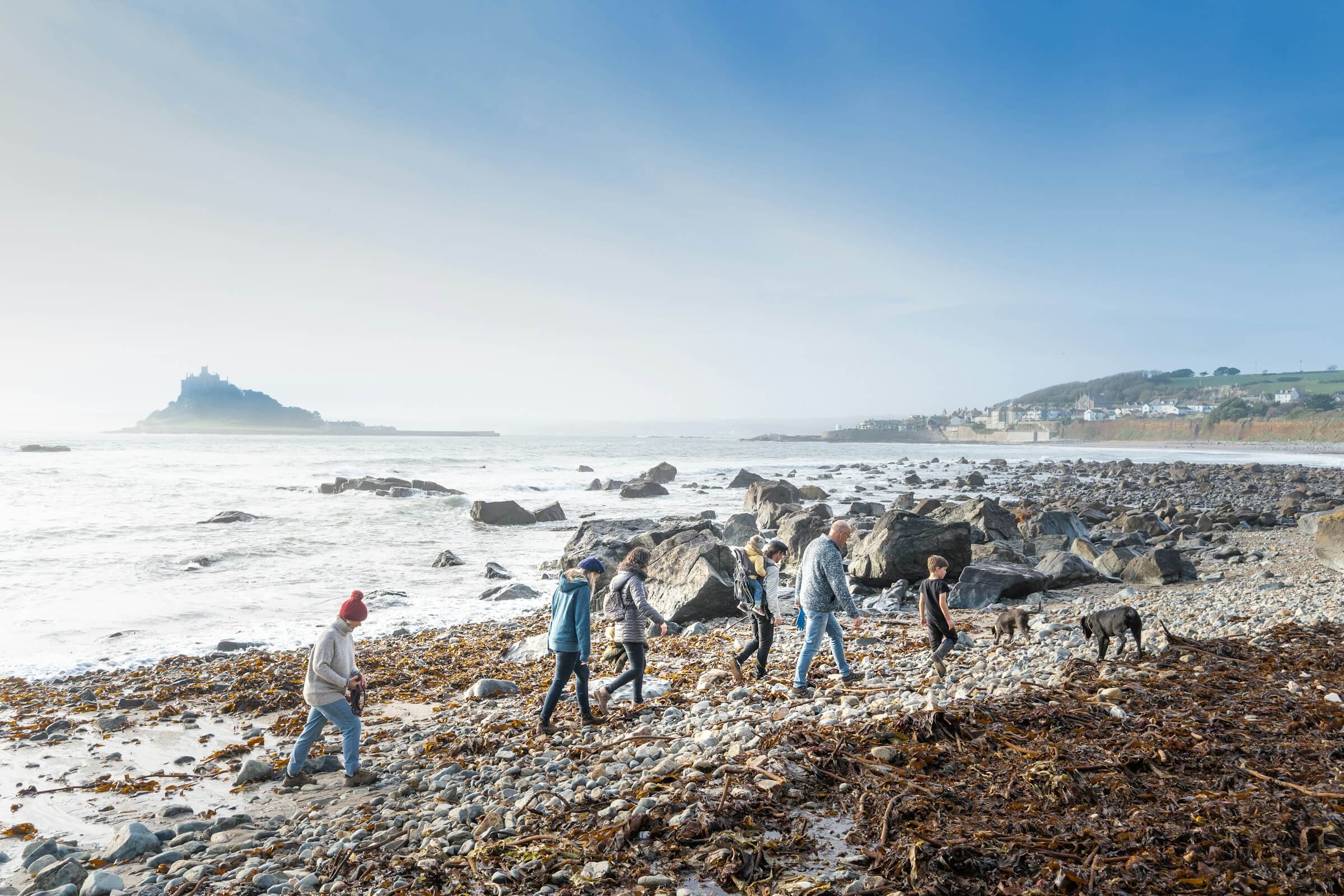 A family walks their dog on a dog friendly beach in Cornwall at Winter