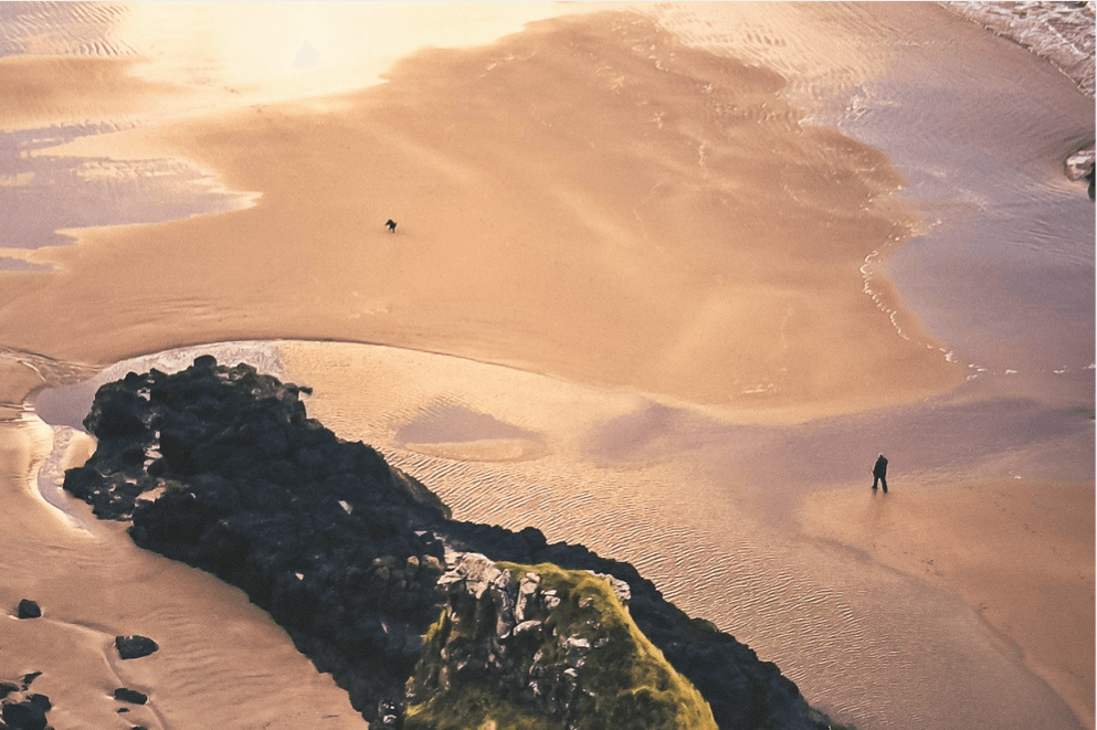 An aeriel shot of a man and his dog playing on a dog friendly beach in Northern Ireland